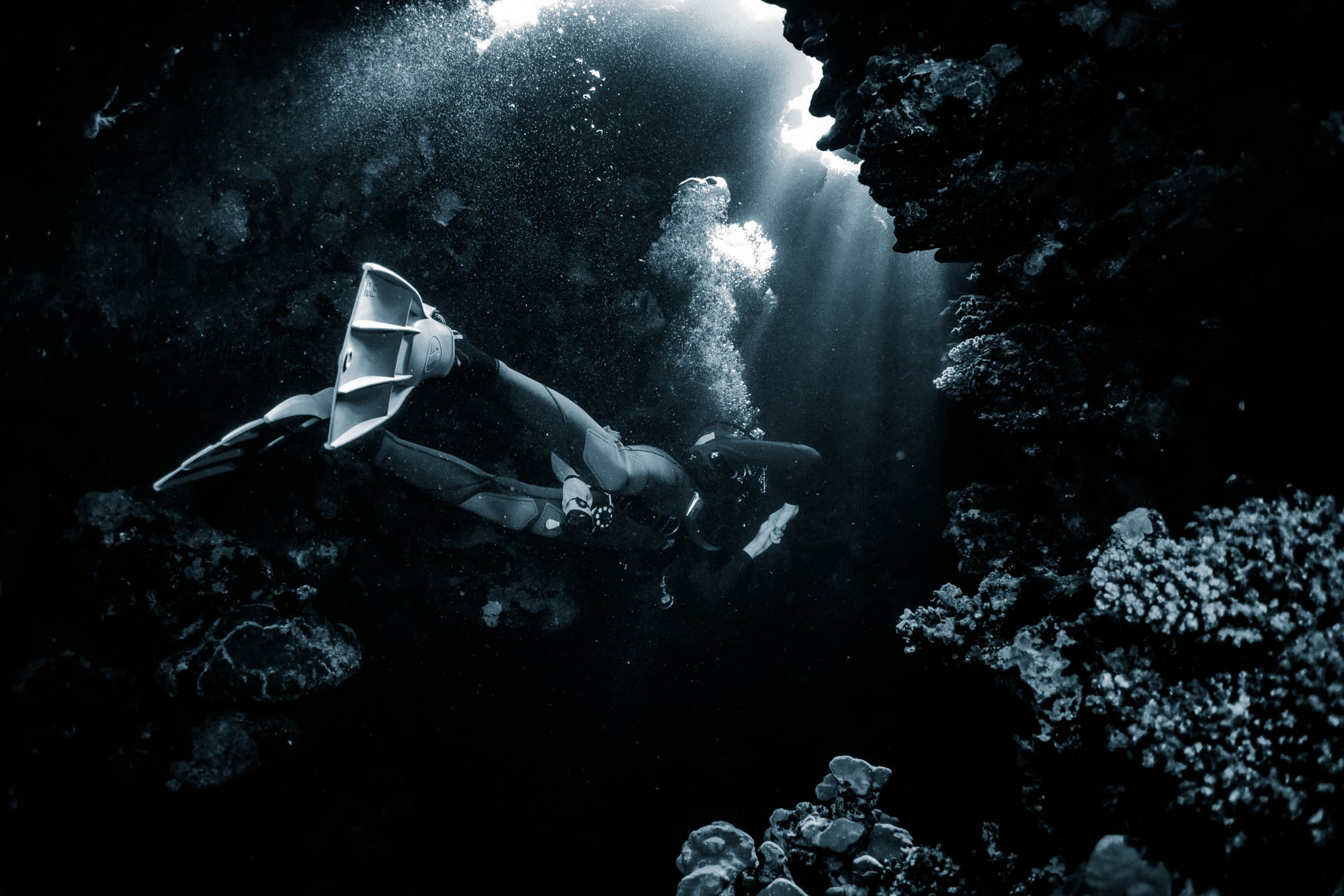 Diver exploring a sunlit underwater cave surrounded by coral formations.