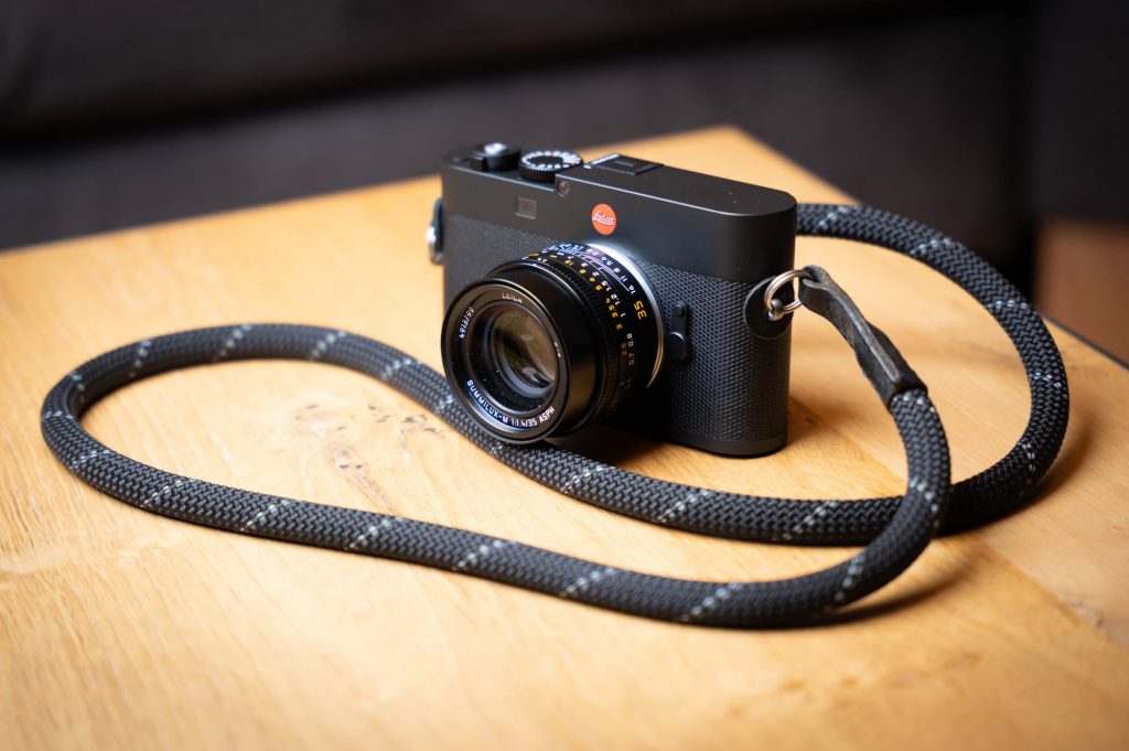 High-end black camera with lens and strap on a wooden table.