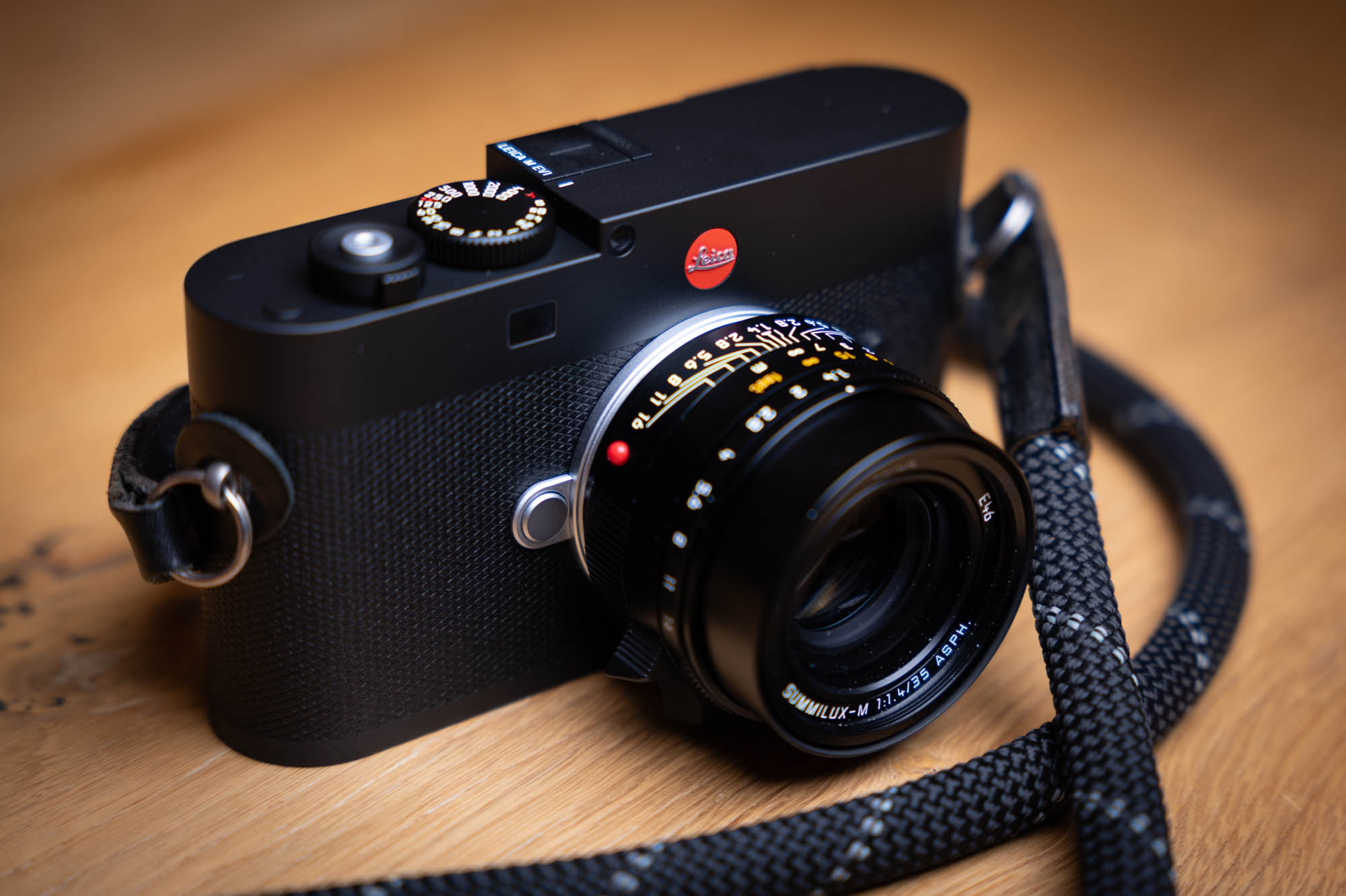 Leica M EV1 camera with lens and strap on a wooden table.